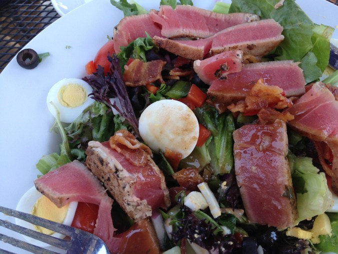 Slices of rare tuna, hard boiled eggs, black olives, and bacon on lettuce.